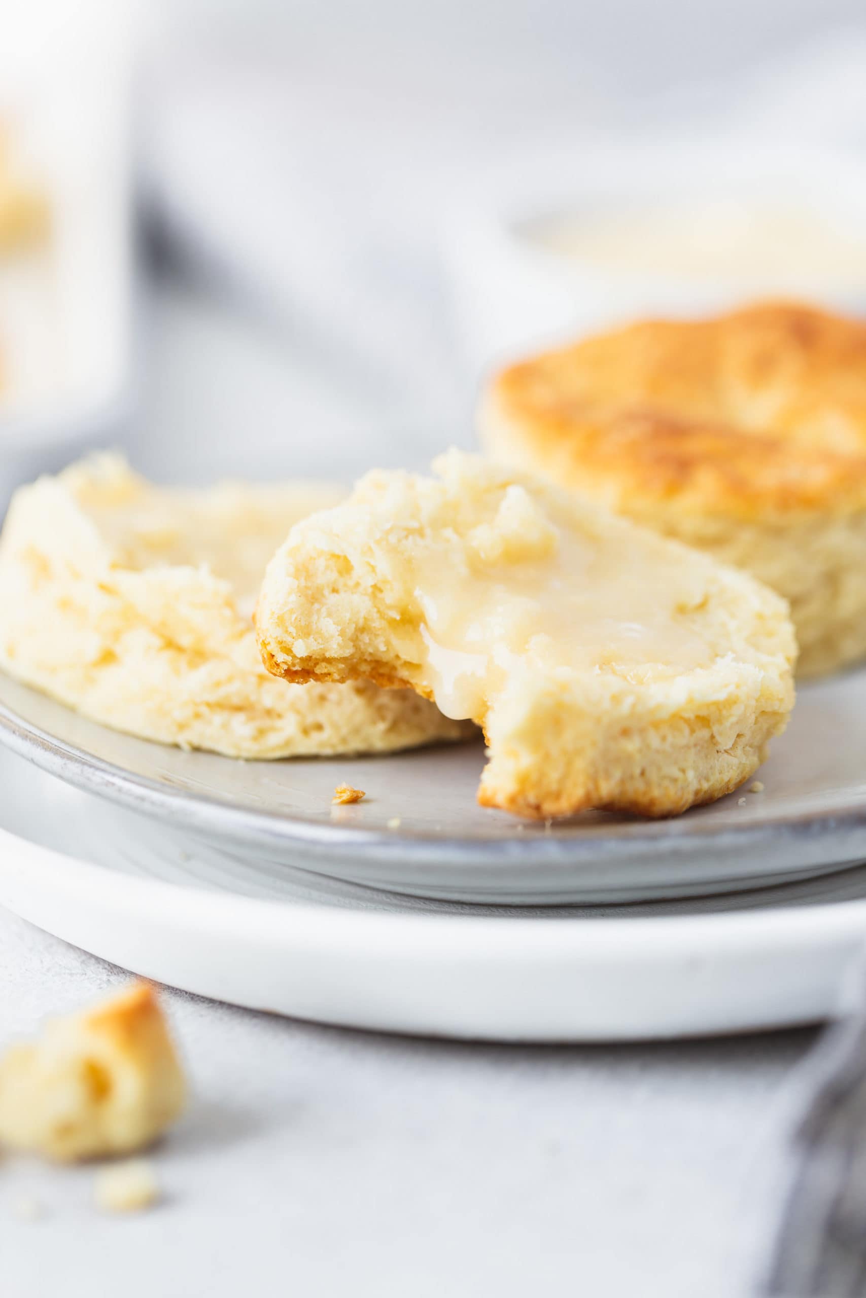 Two buttermilk biscuits on a plate. One biscuit is broken in half and has been spread with honey butter. A bite has been taken from one of the halves.
