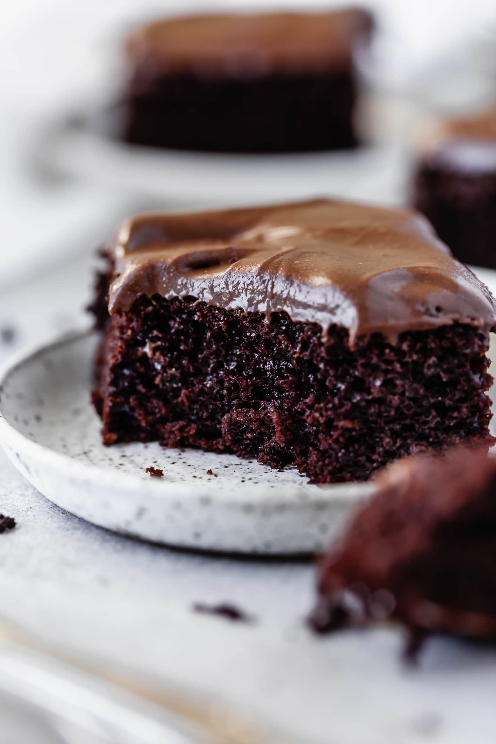 A piece of chocolate mayonnaise cake with chocolate cream cheese frosting. A fork full has been cut off and the fork with cake on it is next to the plate.