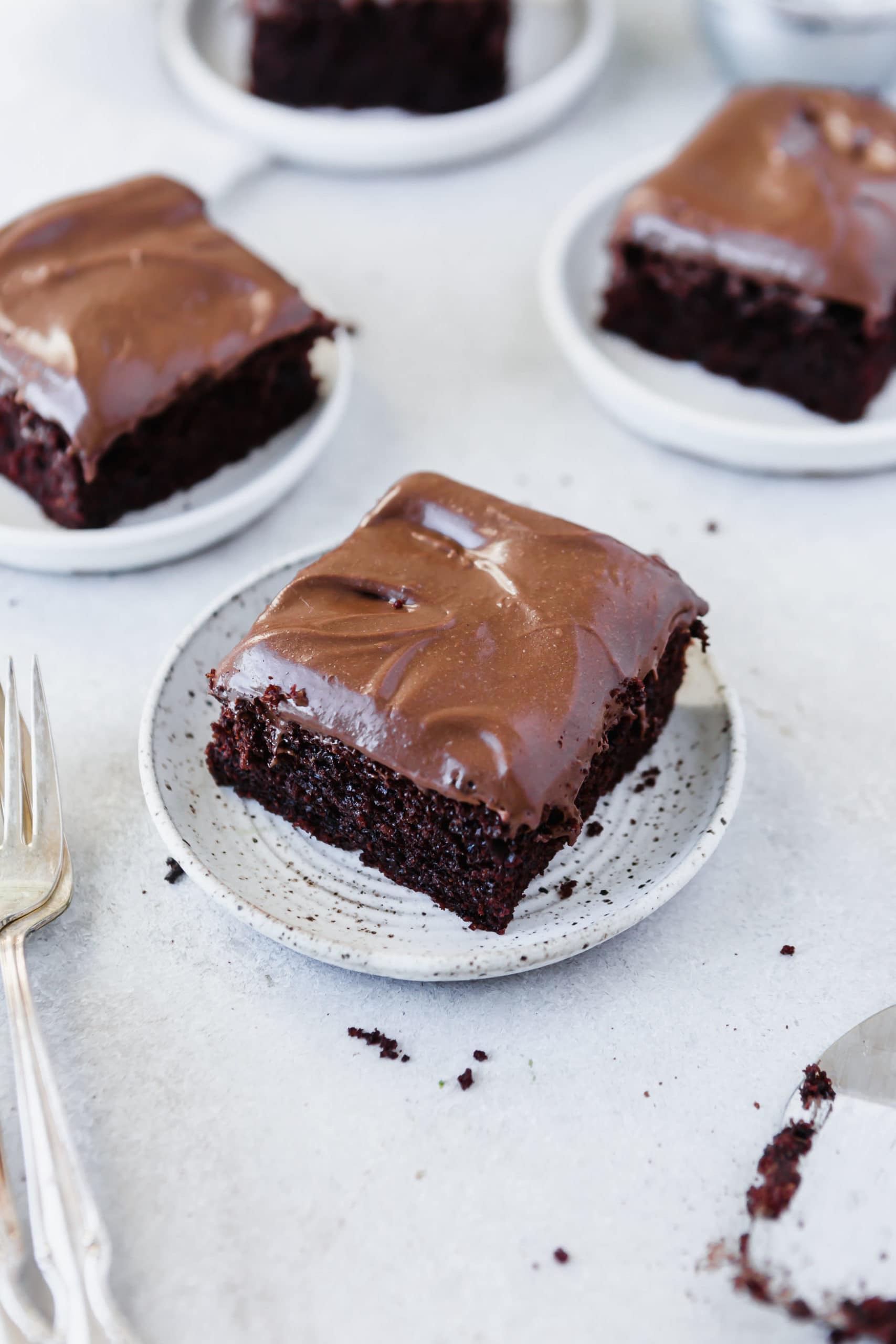 Three white dessert plates each holding a serving of chocolate mayonnaise cake with chocolate cream cheese frosting.