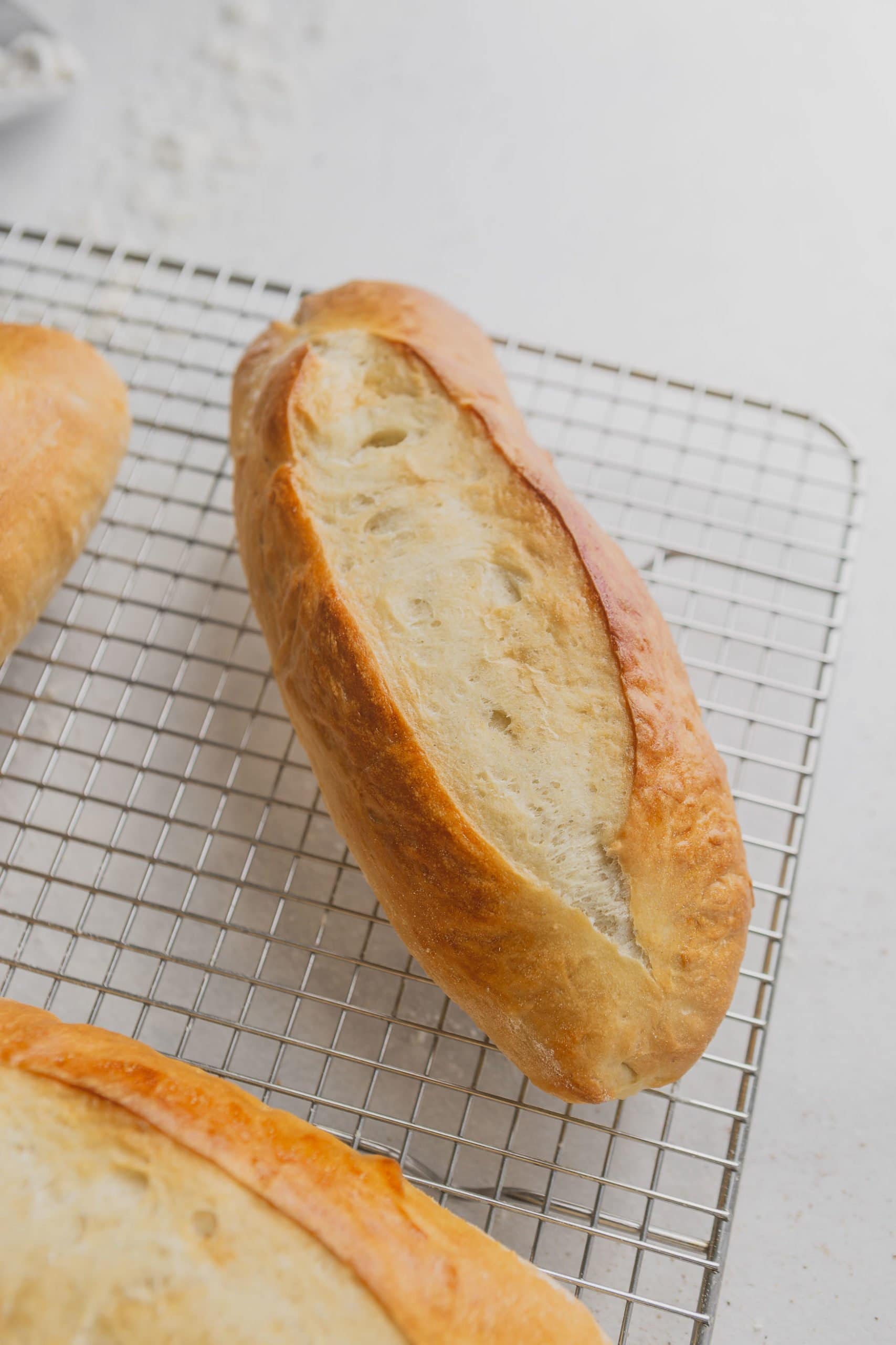 A hoagie roll on a wire cooling rack. the roll is baked to a golden brown.