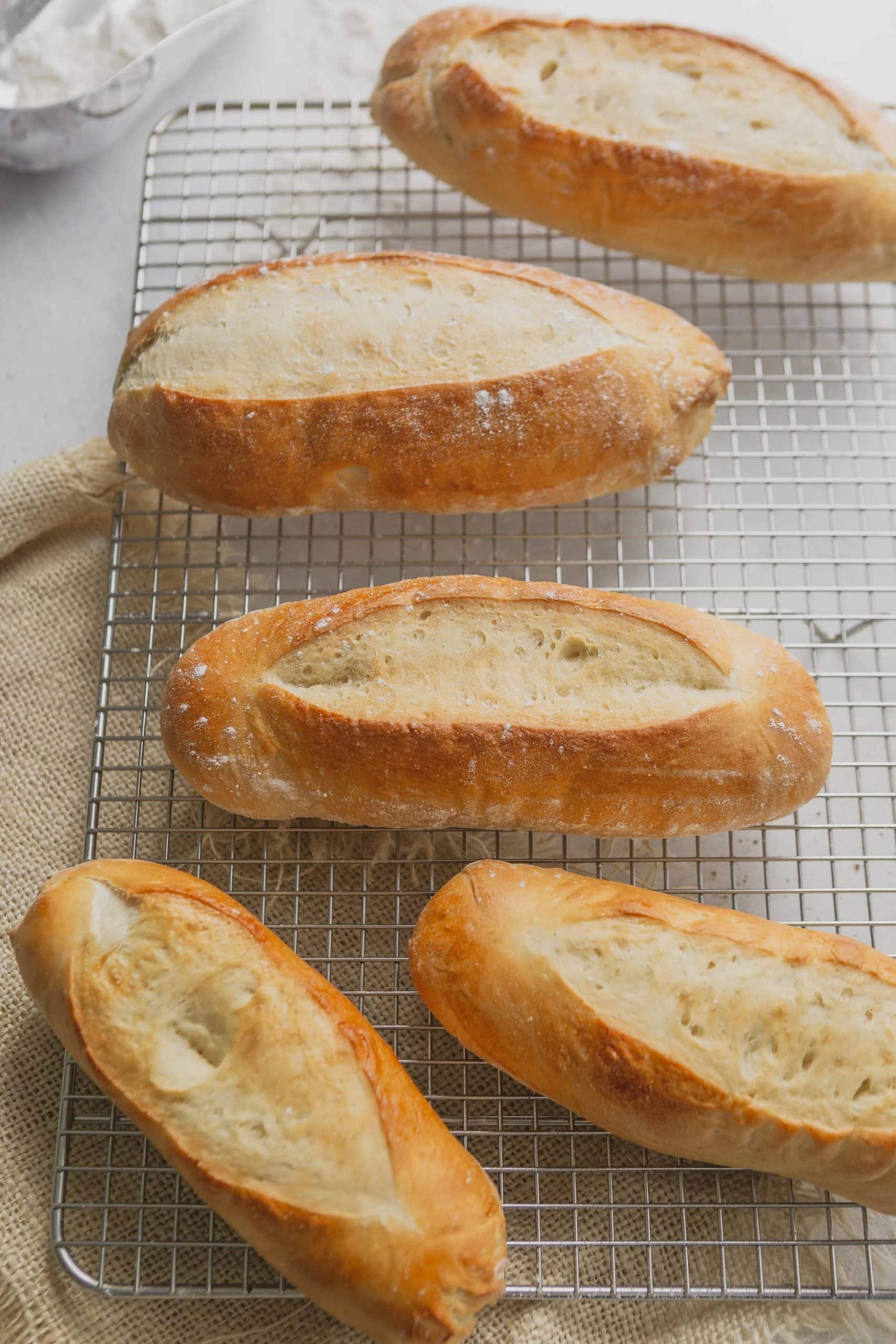 Four hoagie rolls sitting on a wire cooling rack. they are baked to a golden brown.