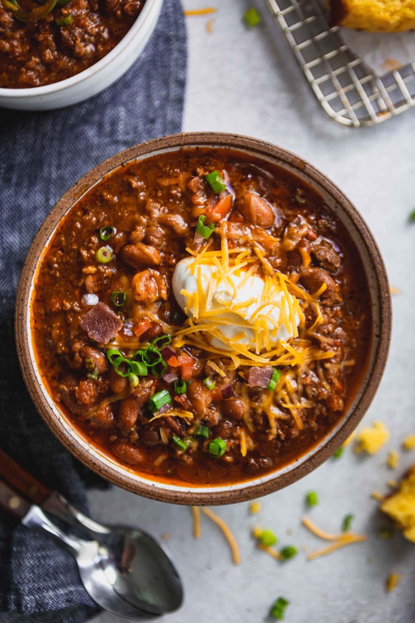 A bowl of the best chili. There is ground beef, three kinds of beans, spices, sour cream and grated cheese on top.