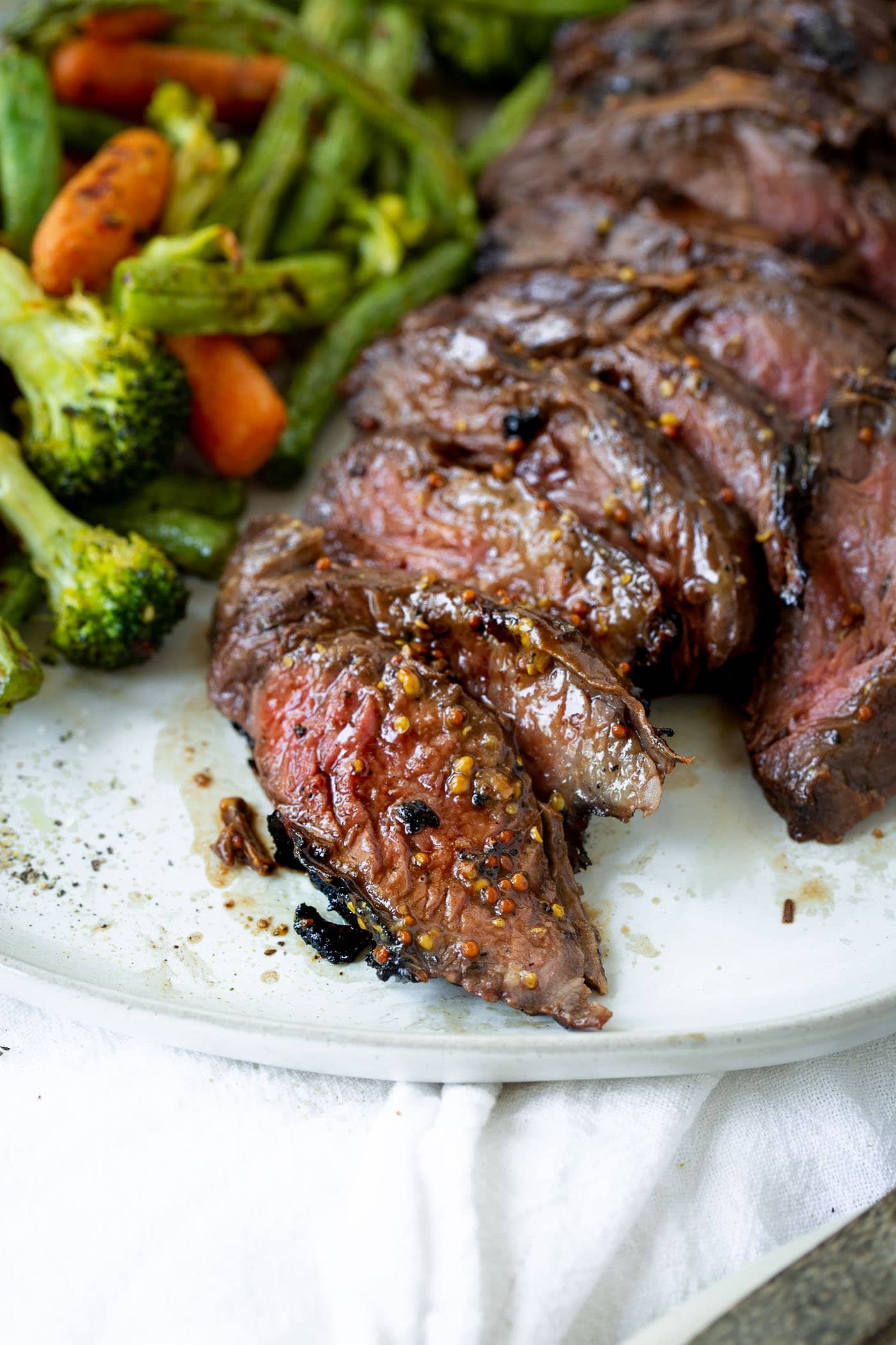 A close up photo of sliced medium rare hanger steak on a white plate next to some roasted vegetables.
