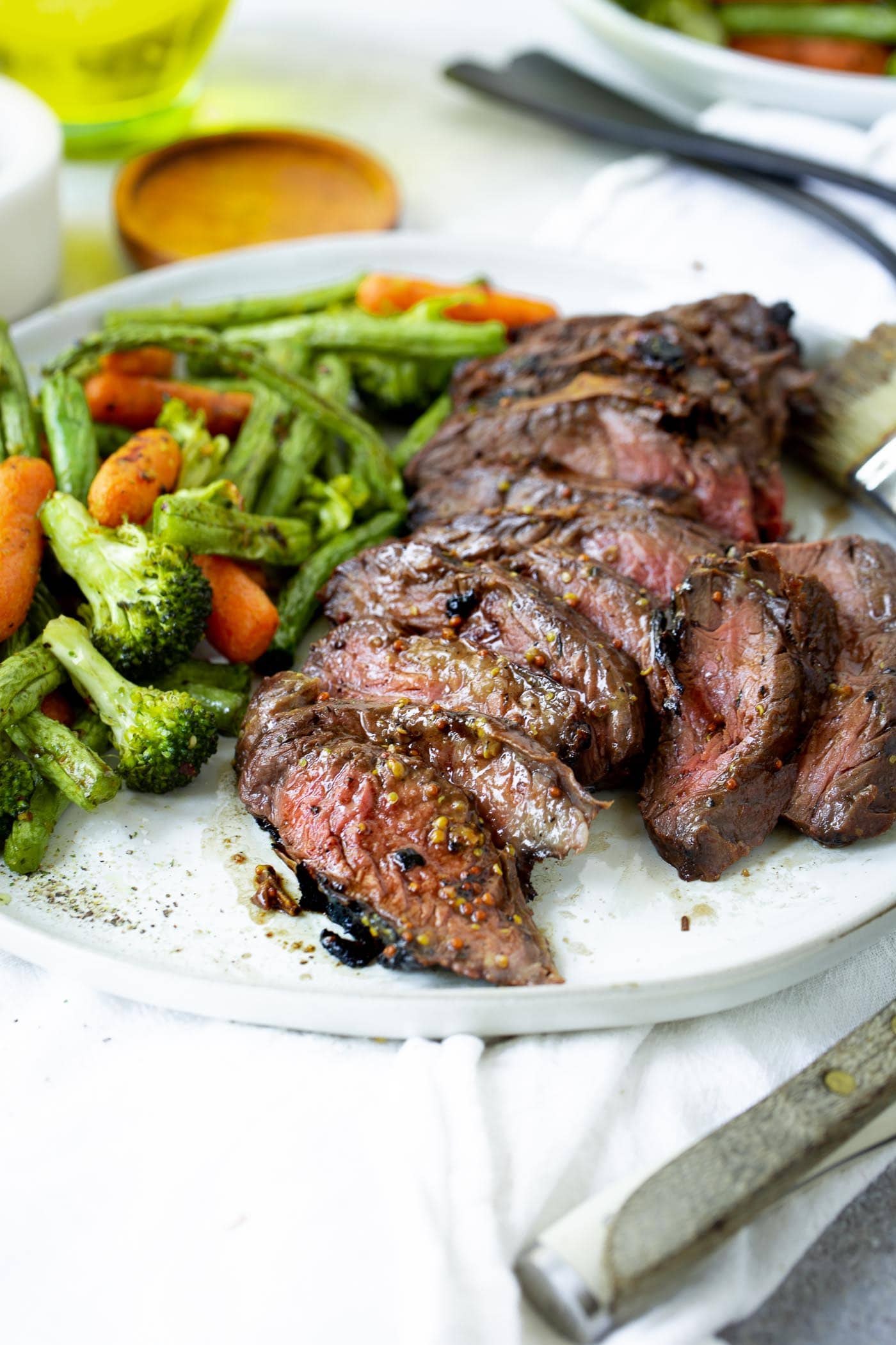 A photo of sliced medium rare hanger steak on a white plate alongside roasted vegetables.